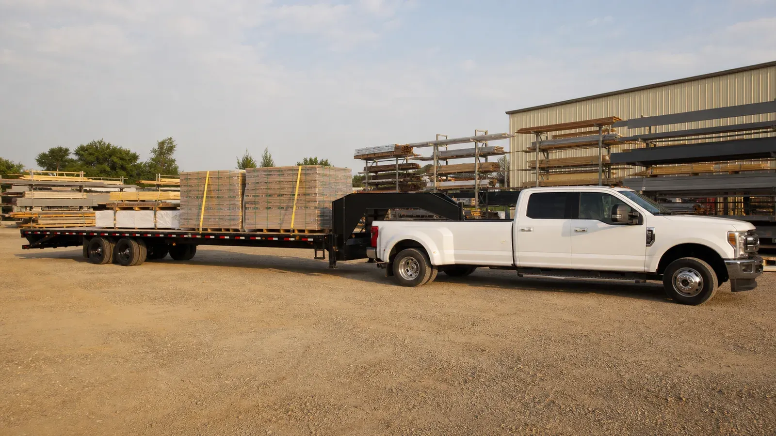 Full-width gooseneck deckover trailer hauling secured construction materials Full-width gooseneck deckover trailer hauling secured construction materials