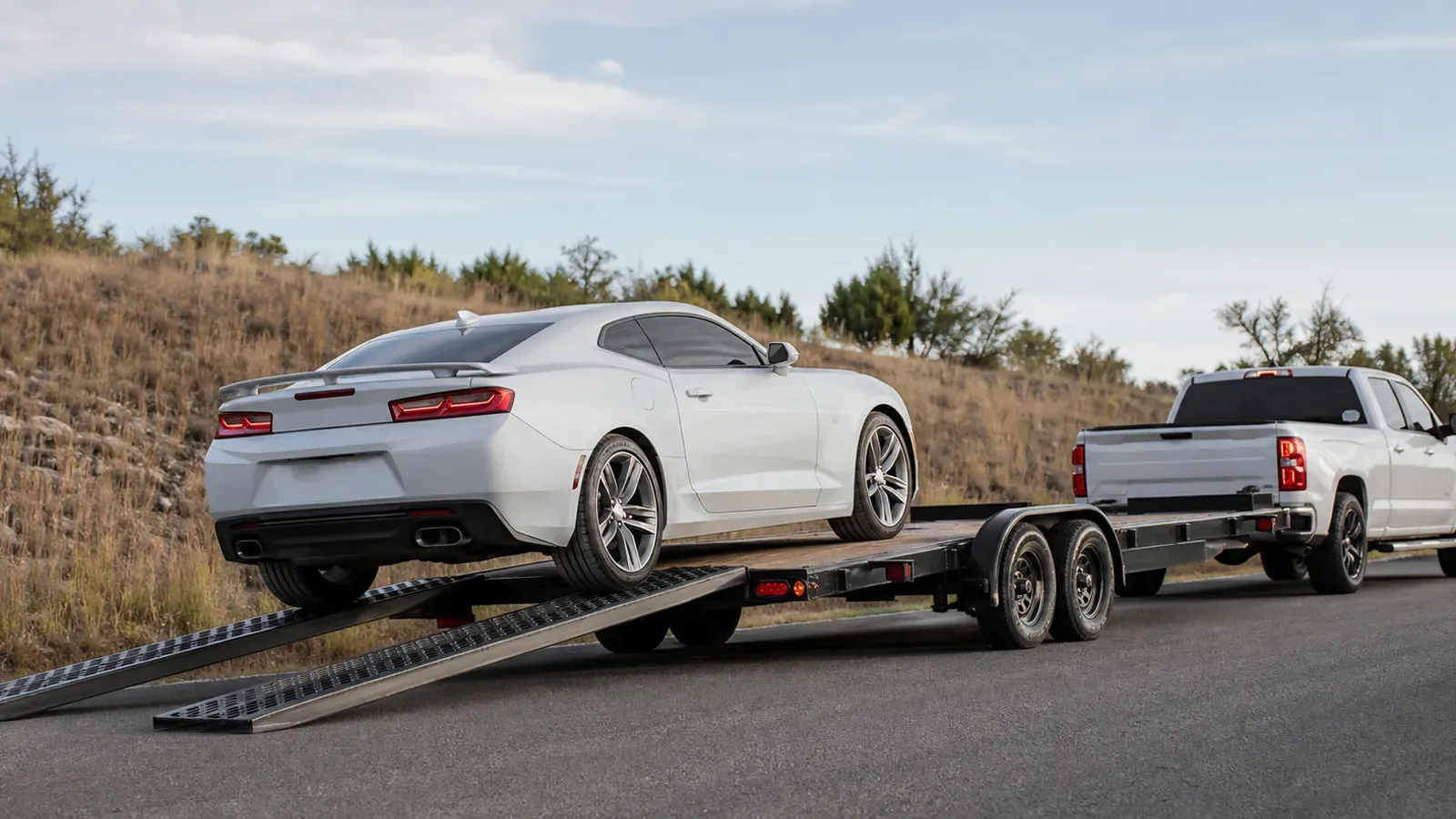Low-profile sports coupe loading onto an open car hauler using long steel ramps